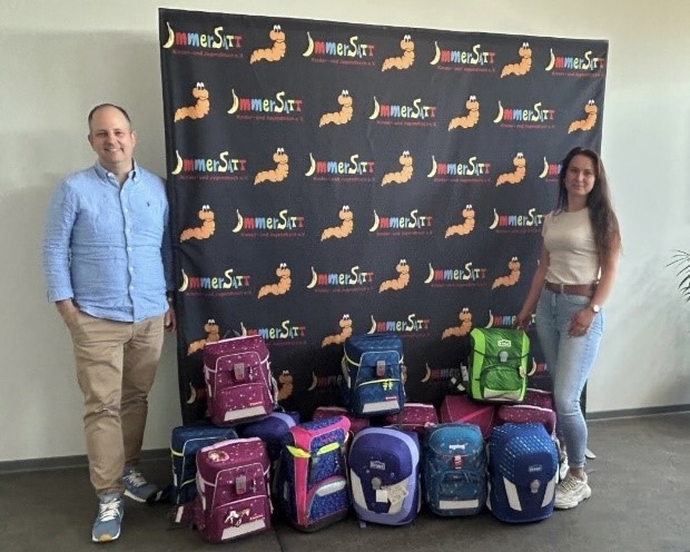 PRA Group European Investments Officer Marcel Köchling and a colleague smiling by a donation of book bags for charity.