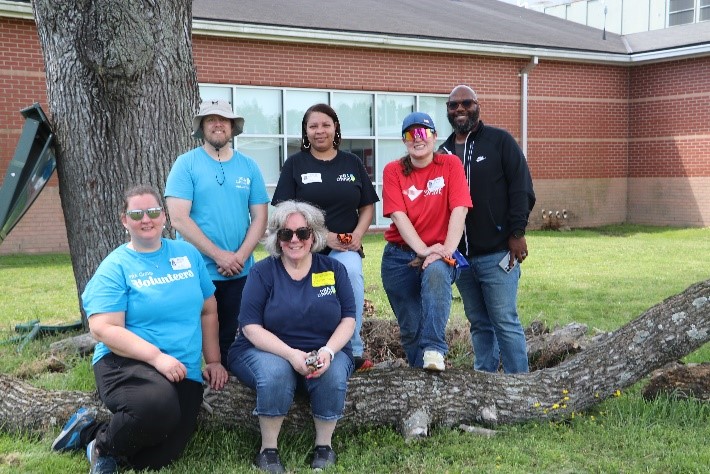 A group of six volunteers smiling while posed around a log.