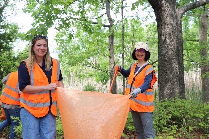 Two volunteers smiling while holding a bag of trash.